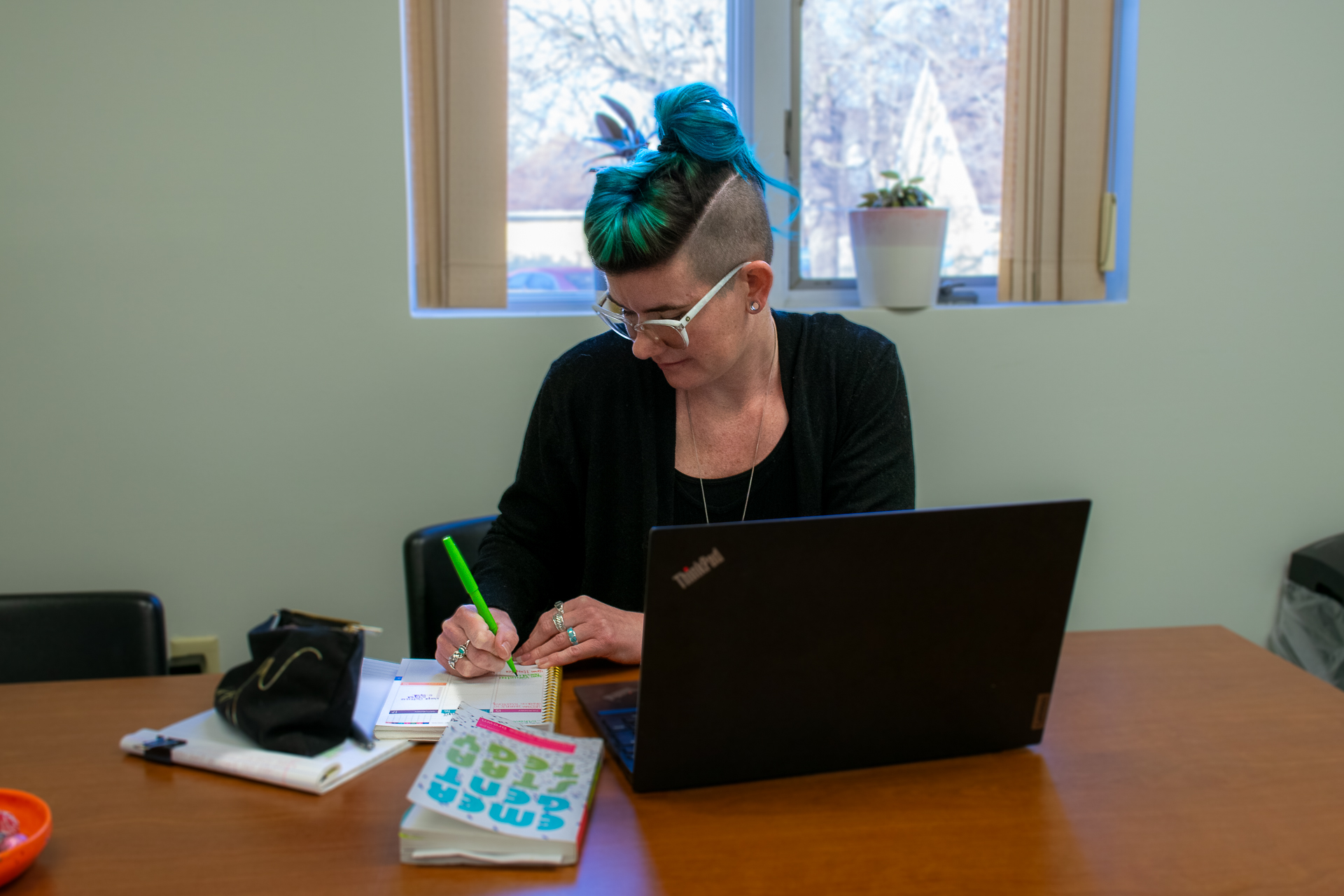 White woman with blue hair working at a table with a laptop