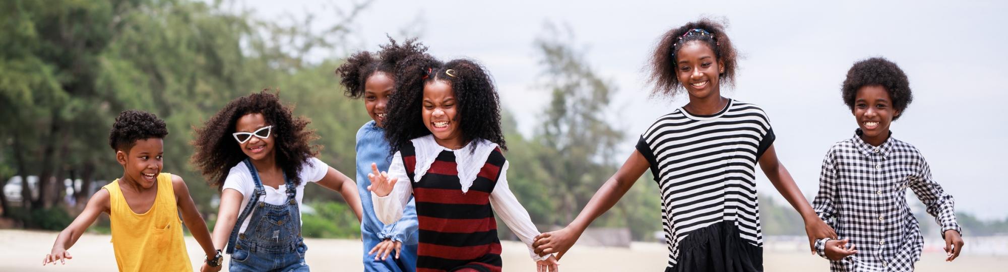 Black children holding hands on beach smiling